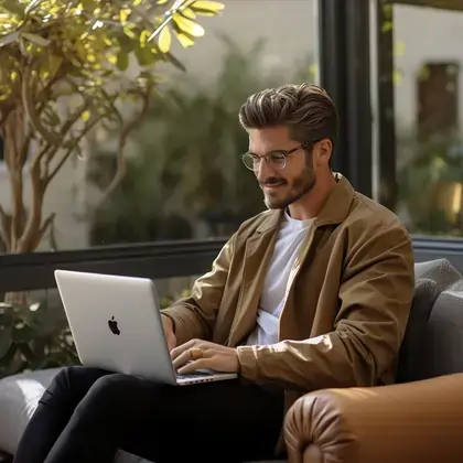 Man in smart casual attire working on a MacBook in a well-lit room, suggesting productivity in a comfortable home environment.