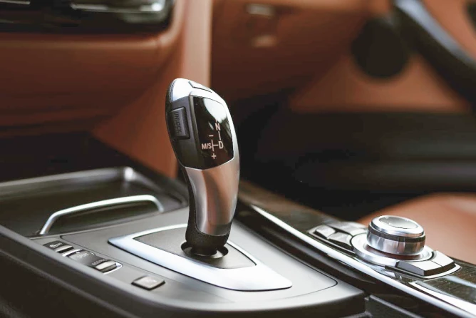 Close-up view of a modern automatic gear shifter inside a luxury car interior with brown leather upholstery and control buttons on the centre console.